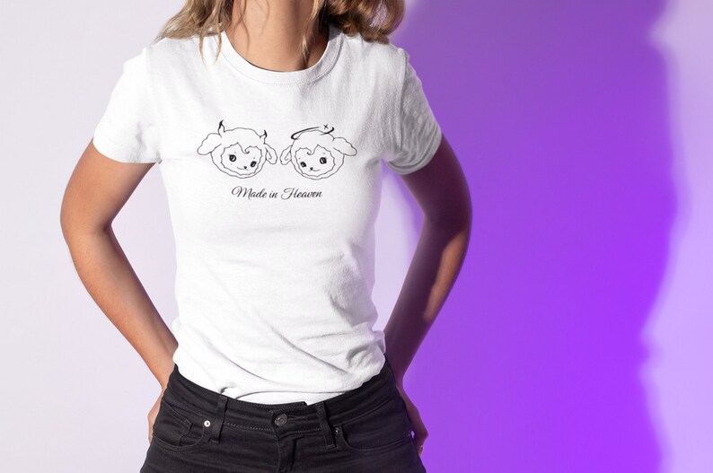 May include: White t-shirt with a graphic of two cartoon sheep, one with devil horns and the other with a halo. The text "Made in Heaven" is printed below the sheep.