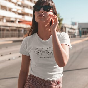 May include: White t-shirt with a black line drawing of two cartoon sheep, one with horns and one with a halo. The text "Made in Heaven" is below the sheep.