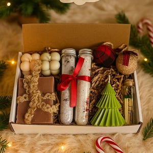 May include: A Christmas-themed gift box filled with various items. The box contains candles, bath salts, soap, and decorative ornaments. A green Christmas tree candle and a candy cane are also visible. The box is presented on a fluffy, white surface.