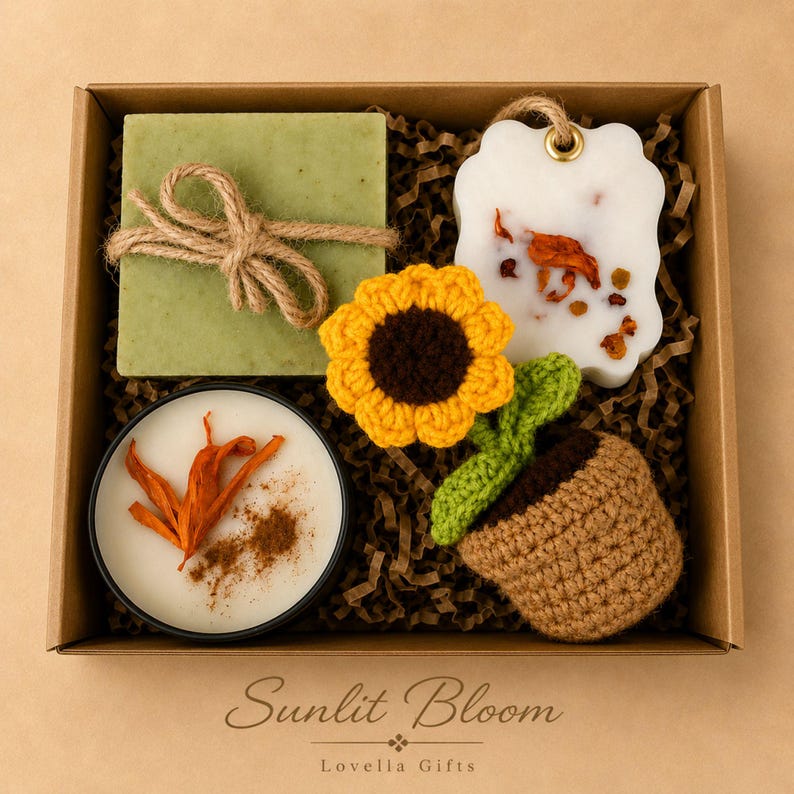 May include: A gift box containing a square green soap wrapped in twine, a white wax melt with dried petals, a round candle with orange peel and cinnamon, and a crocheted sunflower in a brown pot. The box is labelled Sunlit Bloom Lovella Gifts.
