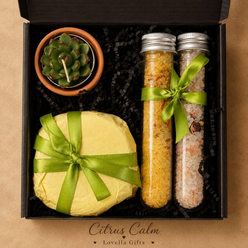 May include: A black gift box containing a succulent-shaped candle in a terracotta pot, a round item wrapped in yellow paper with a green ribbon, and two glass test tubes filled with yellow and pink bath salts, each tied with a green ribbon.