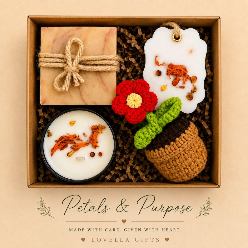 May include: A gift box containing a square marbled soap tied with jute twine, a white wax ornament with dried petals, a round candle with dried orange botanicals, and a crocheted red flower in a brown pot, with text Petals & Purpose.
