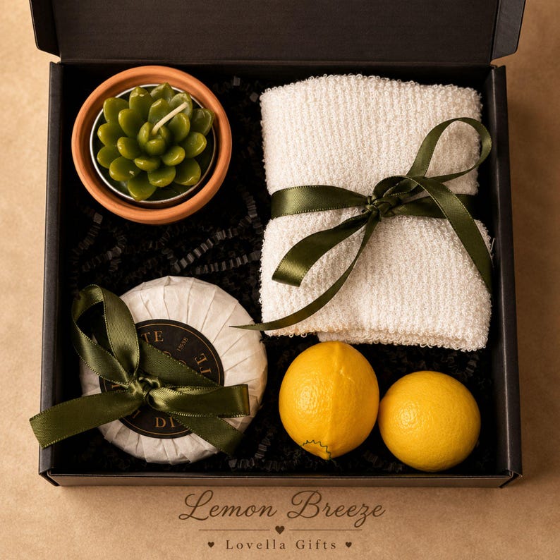 May include: A black gift box containing a green succulent-shaped candle in a terracotta pot, a white textured washcloth tied with a dark green ribbon, a round soap wrapped in white paper with a dark green ribbon, and two bright yellow lemons.