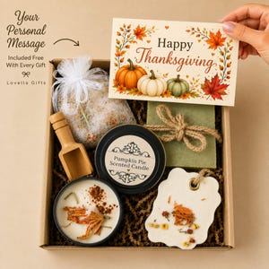 May include: A gift box containing a Pumpkin Pie scented candle in a black tin, a green bar of soap tied with twine, a white wax melt with dried flowers, a wooden scoop, and a bag of bath salts, accompanied by a Happy Thanksgiving card.