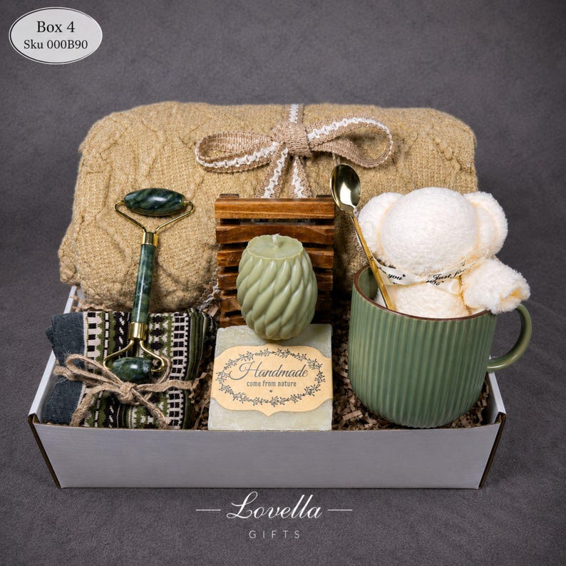 May include: A gift box filled with self-care items. Includes a jade roller, a green mug with a white teddy bear, a candle, soap, a towel, and a wooden soap dish. The box is tied with a bow.