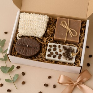 Peut inclure: Coffret cadeau sur le thème du café. Il contient un gant de toilette beige, un savon en forme de grain de café, un pain de savon marron noué avec de la ficelle et un savon blanc décoré de grains de café. Grains de café et ruban éparpillés.