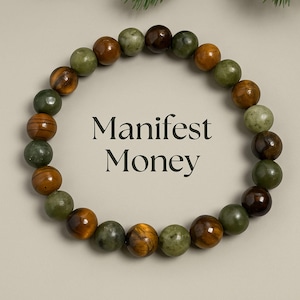 May include: A beaded bracelet with a variety of earth-toned stones, including green, brown, and tiger's eye. The text "Manifest Money" is centered within the bracelet's circular shape. The bracelet is displayed on a neutral background.