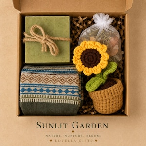 May include: A gift box containing a square green soap bar tied with twine, a pair of folded socks with a blue and brown geometric pattern, and a crocheted sunflower in a brown pot next to a small white organza bag filled with dried botanicals.