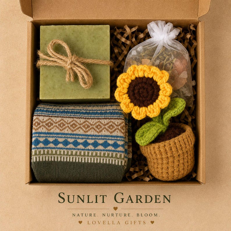 May include: A gift box containing a square green soap bar tied with twine, a pair of folded socks with a blue and brown geometric pattern, and a crocheted sunflower in a brown pot next to a small white organza bag filled with dried botanicals.