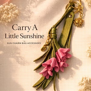 Handmade sunflower bag charm featuring soft pink leather flowers, olive green leather tassel, premium gold sunflower charm and luxury gold hardware. Botanical handbag accessory designed for tote bags, leather handbags, shoulder bags, crossbody bags, straw bags, beach bags and backpacks. Cottagecore purse charm inspired by nature and garden style. Floral bag jewelry, handmade leather keychain, lightweight purse decoration, gift for women, Mother's Day gift, birthday gift, bridesmaid gift.