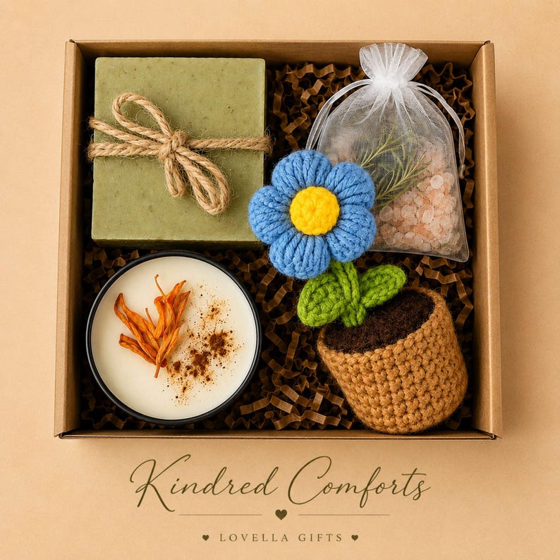 May include: A gift box containing a square olive green soap bar tied with twine, a round candle topped with dried orange peel and cinnamon, a blue and yellow crocheted flower in a brown pot, and a sheer white bag filled with pink bath salts.