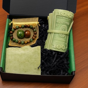 May include: A gift box with a green and black theme. Inside are a green soap bar, a beaded bracelet, a small pouch, and a stack of green money-shaped items. The box is labeled "Box 47".