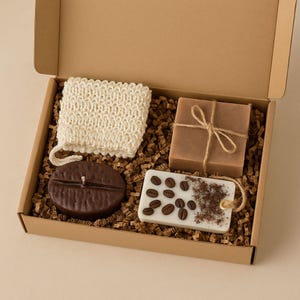 Flat-lay photo of handmade spa set including coffee bean candle, natural artisan soap, exfoliating soap bag, and coffee-scented sachet. Cozy coffee-themed gift box for her, ideal for birthdays, self-care, and thank-you gifts.