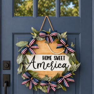 Puede incluir: Una corona patriótica con un letrero de madera que dice "HOME SWEET America". La corona presenta lazos de cinta roja, blanca y azul, vegetación artificial y un collar de perlas, colgada en una puerta azul.