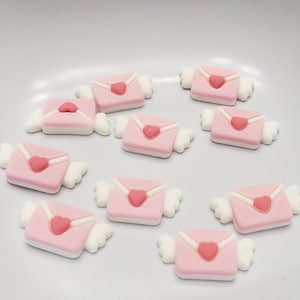 May include: Ten pink and white envelope-shaped charms with a small pink heart on each. The charms have white wings on either side.