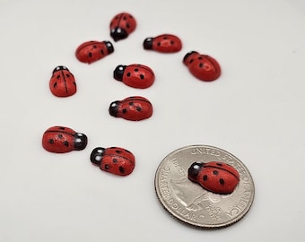 May include: A collection of ten red and black ladybug charms, each with black spots. The charms are approximately the size of a US quarter.