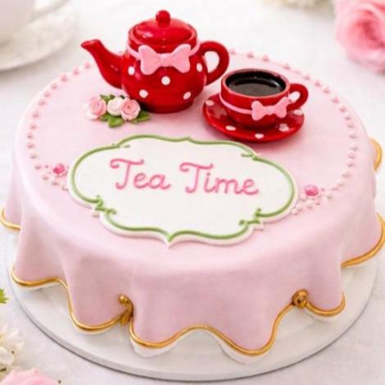 May include: A round cake covered in smooth light pink fondant with a scalloped edge and gold trim. The top features a red teapot with white polka dots and a pink bow, a matching teacup, small pink sugar flowers, and a white plaque reading Tea Time.