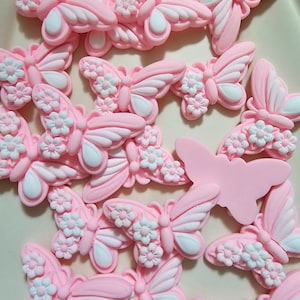 May include: A collection of pink and white butterfly-shaped cake decorations with floral accents. The butterflies have a 3D effect and are perfect for adding a touch of whimsy to cakes and cupcakes.