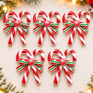 May include: Five identical candy cane ornaments arranged in a group. Each ornament features two crossed candy canes with red and white diagonal stripes, tied together at the center with a green and white striped bow and a small red circular accent.