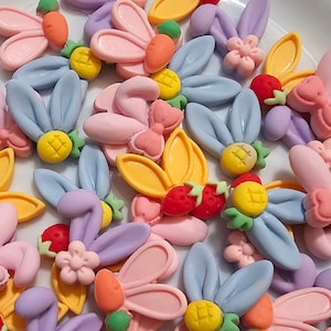 May include: A collection of colorful bunny-shaped resin charms with various designs, including flowers, carrots, pineapples, and strawberries. The charms are perfect for adding a touch of whimsy to crafts and jewelry.