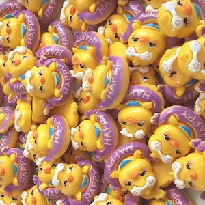 May include: A collection of yellow, cartoon-like figures with purple rings that read "HAPPY". The figures have smiling faces, white accents, and blue details. The image is a close-up, showing many of these figures scattered together.