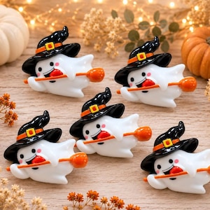 May include: Five small white ghost figurines, each wearing a black witch hat with an orange band and yellow buckle. Each ghost has a smiling face with pink cheeks and is holding an orange broomstick with a round brush end in its arms.