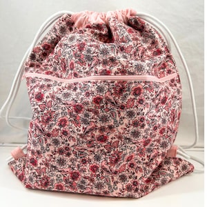 May include: A pink drawstring bag with a floral print and a zippered pocket. The bag has white drawstrings and a white zipper.