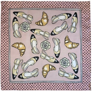 May include: A pink and white patterned silk scarf with a black polka dot border. The scarf features a repeating pattern of black and white shoes, croissants, and white roses.
