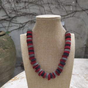 Puede incluir: Un collar hecho de círculos de papel rojo y gris. El collar está en el cuello de un maniquí.
