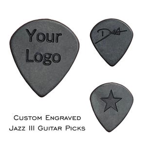 Pode incluir: Três palhetas de guitarra Jazz III cinza escuro. Uma palheta tem "Your Logo" gravado, outra tem uma assinatura e a terceira tem uma estrela. O texto "Custom Engraved Jazz III Guitar Picks" está abaixo.