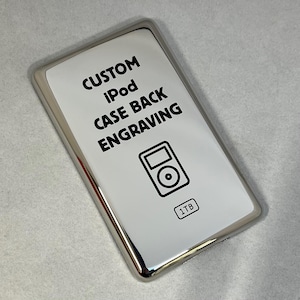 May include: A silver iPod case with a white surface featuring the text "CUSTOM iPod CASE BACK ENGRAVING" and a black iPod graphic. The case also has a "1TB" label.