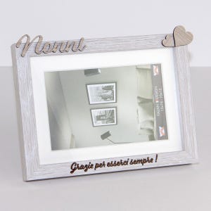 Può includere: Una cornice rettangolare in legno grigio chiaro con un passe-partout bianco. La cornice presenta la parola "Nonni" in corsivo e due cuori in legno. La frase "Grazie per esserci sempre!" è incisa in basso. Contiene una foto.