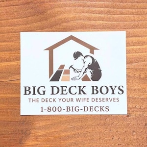 May include: A white rectangular sticker featuring a brown logo of a person building a deck with a hammer. The text reads BIG DECK BOYS, THE DECK YOUR WIFE DESERVES, and 1-800-BIG-DECKS in dark brown lettering centered on the white background.