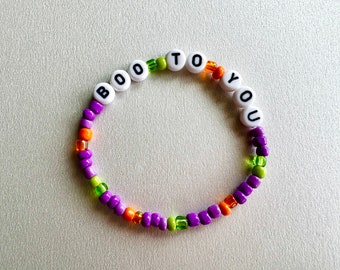 May include: A purple, green, and orange beaded bracelet with white letter beads spelling out "BOO TO YOU".