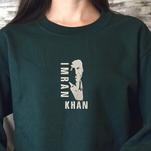 May include: A dark green sweatshirt with a white graphic of a man's face with the text "IMRAN KHAN" printed vertically. The sweatshirt has a white "804" printed on the left sleeve.