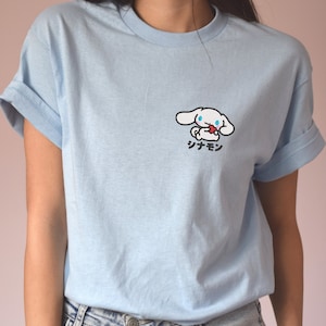 May include: A light blue t-shirt featuring a white cartoon dog holding a red heart. The text "シナモン" is printed below the dog.