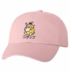 May include: A pink baseball cap featuring a yellow cartoon duck wearing glasses and the Japanese text "コダック" embroidered on the front.