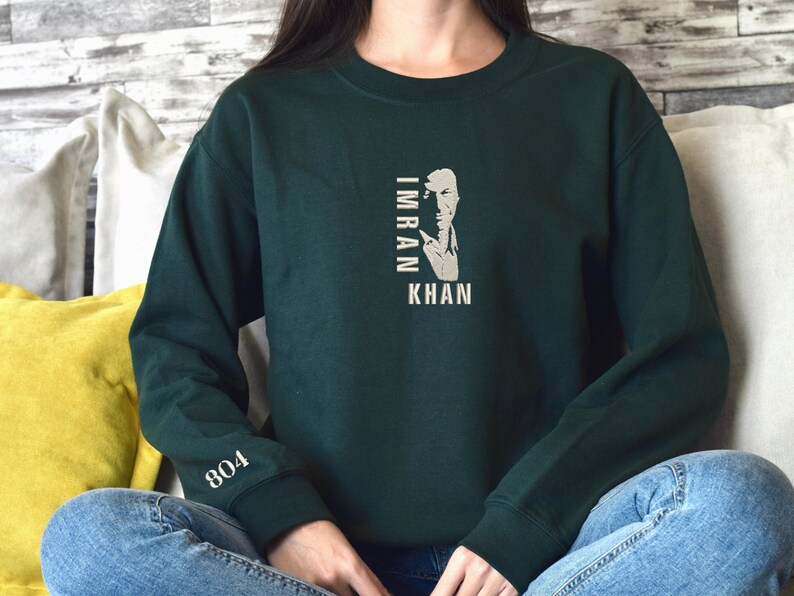 May include: A dark green sweatshirt with a white graphic of a man's face with the text "IMRAN KHAN" printed vertically. The sweatshirt has a white "804" printed on the left sleeve.