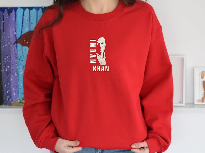 May include: Red sweatshirt with a white graphic of a man's face and the text "IMRAN KHAN" printed on the front.