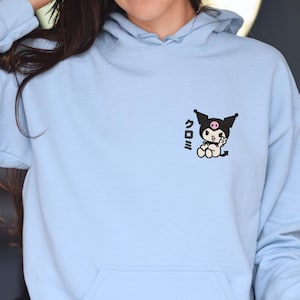 Puede incluir: Una sudadera con capucha azul claro con un gr&aacute;fico en blanco y negro de un personaje de dibujos animados con el texto japon&eacute;s "クロミ" en la parte delantera.