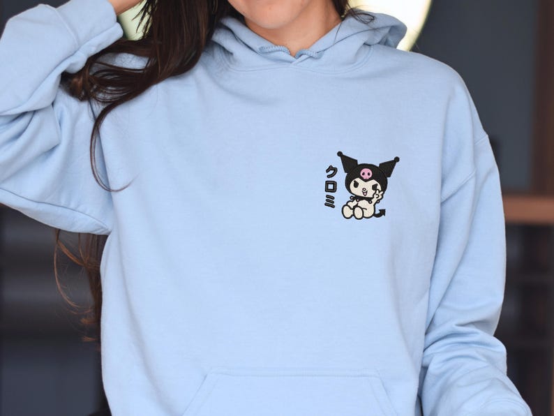 Puede incluir: Una sudadera con capucha azul claro con un gr&aacute;fico en blanco y negro de un personaje de dibujos animados con el texto japon&eacute;s "クロミ" en la parte delantera.