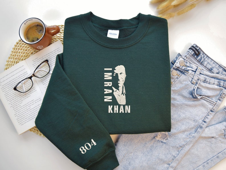 May include: A dark green sweatshirt with a white graphic of Imran Khan's face and the text "Imran Khan" printed vertically. The number "804" is printed on the left sleeve.