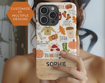 May include: A white phone case with a wood-grain bottom. The case features a colorful autumn-themed design with pumpkins, leaves, boots, and the text "Autumn Vibes", "Stay Cozy", and "Thankful". The name "Sophie" is printed on the wood-grain bottom.