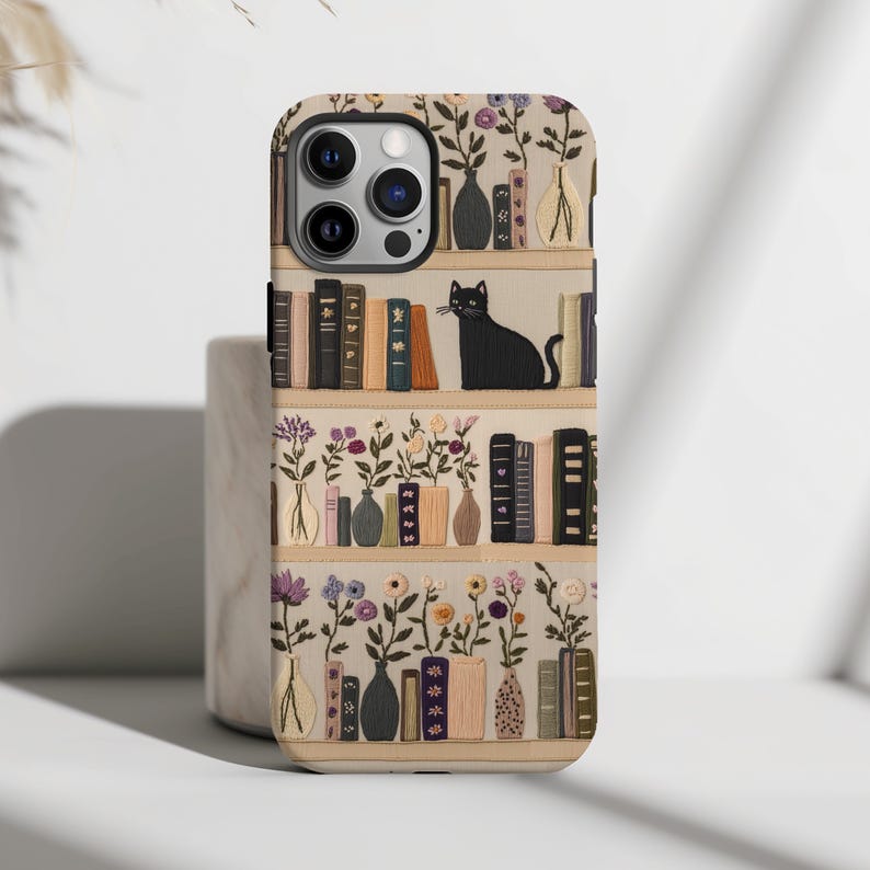 Embrace books and nature with our Bookish Boho Floral Phone Case.  Designed with book lovers in mind, this faux embroidery cat on bookshelf phone case features a flat surface print of shelved books, a cat and flowers on a vintage look background