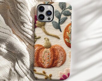 May include: A phone case featuring an embroidered design with a pumpkin, flowers, and leaves in shades of orange, green, and pink. The case has a cream-colored background and a textured appearance, suggesting a fabric-like material.