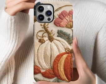 May include: A smartphone case featuring an embroidered design of a large white pumpkin and a smaller orange pumpkin. The pattern includes pink flowers, green leaves, and brown vines on a cream-colored background, with a black camera cutout.