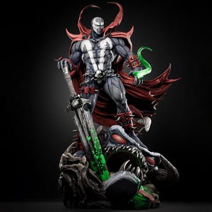 May include: A detailed statue of Spawn, a comic book character, standing on a grotesque creature. The figure is predominantly gray and black, with a white chest emblem, red cape, and spiked accents. He holds a large sword and a green energy effect.