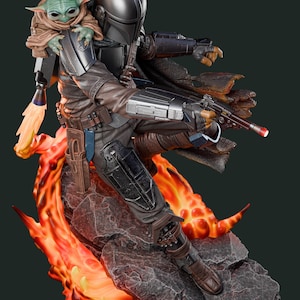 May include: A detailed figurine of The Mandalorian with Grogu, posed dynamically on a rocky base with fiery accents. The Mandalorian is clad in dark armour, holding a blaster, with Grogu perched on his shoulder. The base features vibrant orange and red flames.