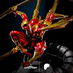 以下が含まれることがあります： 赤と金の姿の、しゃがんだポーズの、スパイダーマンのアクションフィギュア。フィギュアは、背中から伸びる複数の金色の機械的な腕を持っています。フィギュアは、Epic Propのロゴが見える、グレーと黒のテクスチャベースにあります。