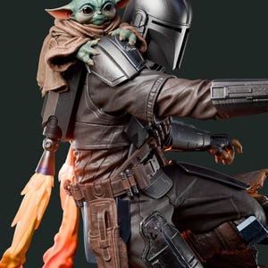 May include: A detailed figurine of The Mandalorian with Grogu. The Mandalorian is wearing a silver helmet and brown armour. Grogu, also known as Baby Yoda, is perched on his shoulder. A flame effect emanates from the jetpack.